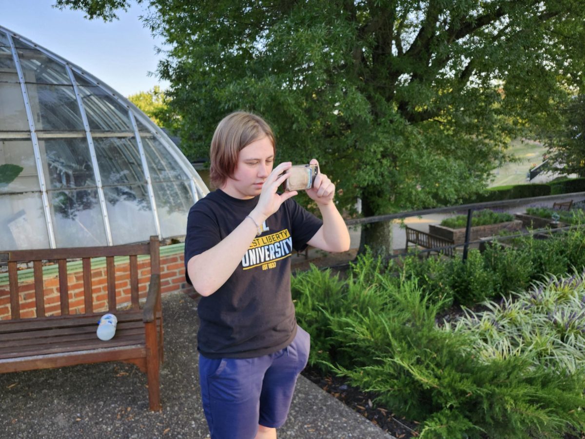 Student taking a photo in front of greenhouse with their phone
